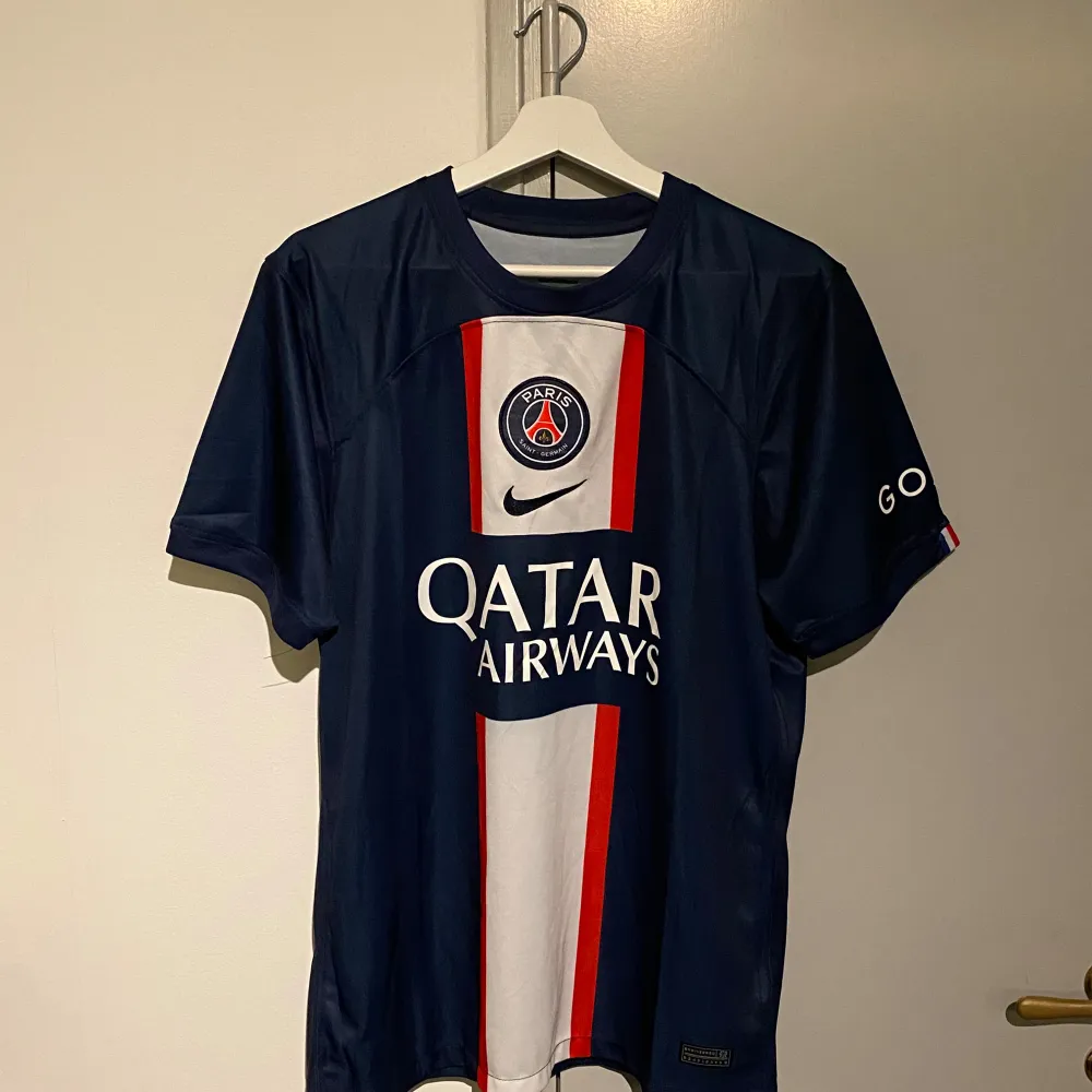 Säljer en snygg PSG fotbollströja i blått med Mbappé och nummer 7 på ryggen. Tröjan har korta ärmar och är i mycket bra skick. Den har vita och röda detaljer samt Qatar Airways som sponsorlogga på framsidan. Perfekt för alla PSG-fans!. T-shirts.