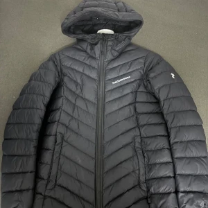 Svart dunjacka från Peak Performance - Säljer en svart dunjacka från Peak Performance i mycket bra skick. Jackan har en snygg quiltad design med dragkedja och huva. Perfekt för kalla vinterdagar och håller dig varm och bekväm. Passar både till vardags och utomhusaktiviteter.