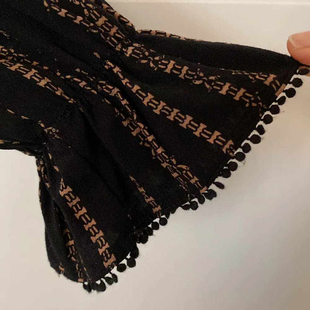 Snygg svart klänning med beigerandigt mönster från Designers Remix. Den har långa ärmar med fina detaljer vid ärmsluten och ett knytbälte i midjan för fin böljande passform. Perfekt för höst, vinter och vår!. Mekot.