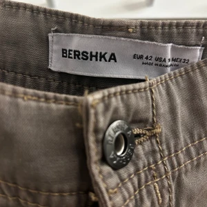 Bruna cargobyxor från Bershka - Säljer ett par snygga bruna cargobyxor från Bershka i storlek EUR 42. Byxorna har en loose passform med stora fickor på sidorna och en knappdetalj. Perfekta för både vardag, lite finare tillfällen och passar bra till höstgarderoben. Mid waist