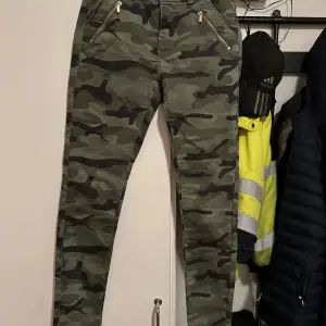 Säljer ett par coola kamouflagefärgade byxor från H&M i storlek 152. Byxorna har dragkedjor vid fickorna och en knapp i midjan. Perfekta för en avslappnad och trendig look. Passar bra till både vardag och äventyr!