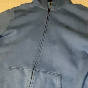Blå hoodie från Polo Ralph Lauren - Säljer en snygg blå hoodie från Polo Ralph Lauren i bra skick. Den har en dragkedja framtill och en liten logga på bröstet. Perfekt för höst och vår, och den är superbekväm med sin mjuka insida. Passar perfekt för en casual look eller när du bara vill mysa hemma. 🌀 Ordinare pris 1300kr