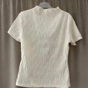 Vit topp med ditaljer - Säljer en jättefin topp, den har en tajtare passform med snygga ditaljer på! vet inte vart den är ifrån då jag någongång klippt bort lappen och minns tyvärr inte🙃