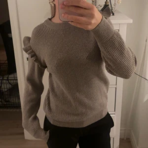 Beige stickad tröja med volangdetaljer - Säljer en superfin beige stickad tröja med volangdetaljer på axlarna. Perfekt för höst och vinter! Tröjan har långa ärmar och en bekväm passform. Den är både stilren och mysig, perfekt för kalla dagar. Hör av dig vid intresse! 🍂