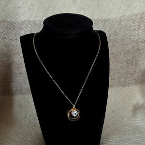 Guldigt halsband med glittrig sten - Snyggt halsband med en glittrig sten i mitten, omgiven av en guldfärgad ram.⚜️💎🩷 Defekt: tappat lite färg på den guldiga ramen