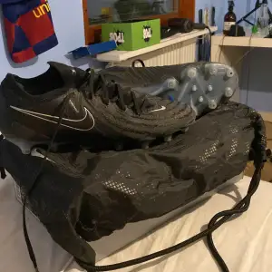 Säljer ett par svarta Nike Phantom fotbollsskor i bra skick. Skorna har en snygg design med blå detaljer och är perfekta för fotbollsträning. De har en robust sula med dobbar för bra grepp på planen. Kommer med og förvaringspåse och låda. Självklart äkta.