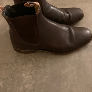 RM williams boots  - Säljer ett par klassiska bruna Chelsea boots från R.M. Williams i skinn. De har en stilren design med elastiska paneler på sidorna och en låg klack. Perfekta för både vardag och fest. Skorna är i bra skick med lite slitage på tån.