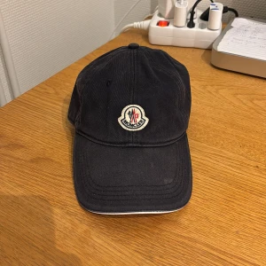  Moncler keps - Säljer en snygg svart keps från Moncler med deras ikoniska logga framtill. Köpt på NK, nypris: 2000kr. Mitt pris: 699.  Kvitto kan finnas. Pris kan diskuteras vid snabb affär. 
