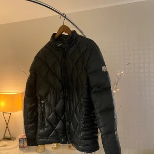 Svart quiltad dunjacka från Moncler - Säljer en snygg svart quiltad dunjacka från Moncler. Jackan har en dragkedja framtill och är perfekt för kyliga dagar. Den är i mycket bra skick och har långa ärmar. Passar perfekt för höst och vinter. Perfekt för dig som vill hålla stilen i kylan! 🖤4 motsvarar storlek M-L