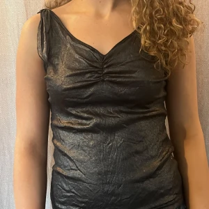 Svart glittrig topp från Un Jour Ailleurs - Snygg svart glittrig topp från Un Jour Ailleurs i ett glansigt material. Köpt på Humana