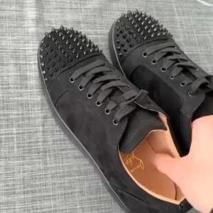 Christian louboutin - Säljer ett par svarta sneakers med coola nitar på tån och snörning. De har en ikonisk röd sula som verkligen sticker ut. Perfekta för att ge din outfit en edgy touch!