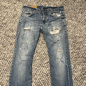 Dondups - Säljer ett par coola blå jeans från Dondup med en riktigt sliten look. De har flera hål och slitningar både fram och bak, vilket ger dem en edgy stil. Perfekta för en avslappnad och trendig outfit. Passar bra till sneakers eller boots! Nypris 3299kr