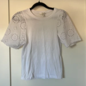 T-shirt med detaljer - Jättesöt t-shirt från HM med blomdetaljer på ärmarna. Använd väldigt lite och har inga fläckar eller defekter. Skriv för bilder eller vid intresse.