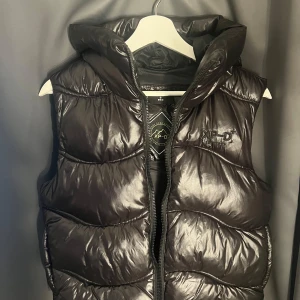 Väst - Nu säljer jag min svarta glansiga superdry väst då den är för liten, själv tycker jag den är liten i storleken. Nästan oanvänd och inga tecken på skador!!