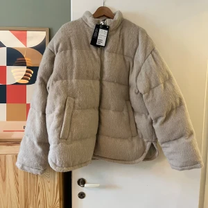 Beige pufferjacka från Weekday - Säljer en supermysig beige pufferjacka från Weekday. Den är perfekt för kyliga dagar med sitt fluffiga och quiltade material. Jackan har en dragkedja framtill och två praktiska fickor. Den är i storlek L men är stor i storlek så snarare XL.