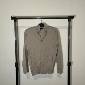 Beige merinoulltröja från MNG - Säljer en stilren beige tröja i merinoull från MNG. Tröjan har en dragkedja vid halsen och långa ärmar. Perfekt för kyligare dagar.