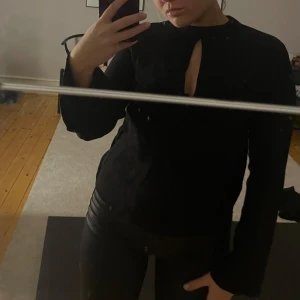 Svart långärmad topp med öppning - Snygg svart långärmad topp med en unik öppning framtill och baktill. Perfekt för en stilren look. Passar bra till både jeans och kjol.