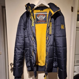 Snygg vinterjacka från Carbonz - Snygg och varm vinterjacka från Carbonz. Storlek XL. Knappt använd. Hel o ren. Färgen är typ svart/mörkblå.