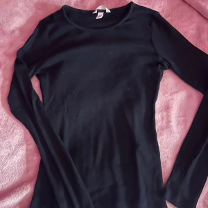 Svart ribbad långärmad tröja - Snygg svart ribbad tröja med långa ärmar. Perfekt för lager-på-lager eller som den är. 