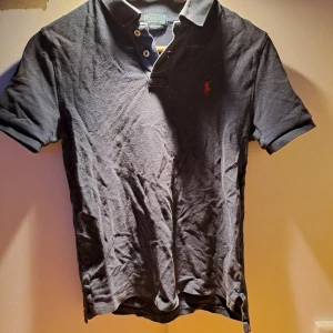Ralph Lauren Piké - Säljer en klassisk och sjuukt fet mörkblå pikétröja från Ralph Lauren med den ikoniska loggan broderad i rött på bröstet. Tröjan har korta ärmar och en stilren krage. Passar främst kids. Perfekt för en avslappnad men stilfull look. Skick är väldigt bra endast skrynklig men det kan lösas innan frakt. Modellen är 175 och väger ca 65.Hör av er vid frågor