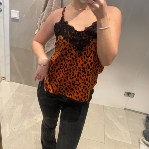 Leopardmönstrad linne med spetsdetaljer - Snygg leopardmönstrad linne i orange och svart med spetsdetaljer vid halsringningen. Perfekt för en trendig look.