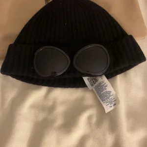 Cp company mössa - Snygg svart stickad mössa från C.P. Company med unika glasögondetaljer framtill. Mycket skön och varm nu på vintern. Nypris 1500kr