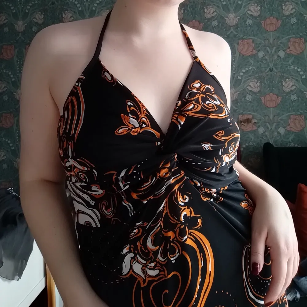 Vintage svart halterneck-klänning med ett coolt unikt mönster i orange och vitt. Klänningen har en twisdesign framtill. Superskön och sval🩷. Mekot.
