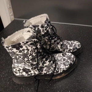 Svartvita blommiga kängor med snörning - Snygga kängor med ett unikt svartvitt blommönster. De har snörning framtill och en robust sula som ger bra grepp. Sparsamt använda. Tvättar såklart innan jag skickar dem.