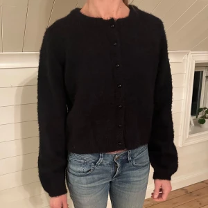 Svart kofta från Pieces - Mysig svart kofta från Pieces med knappar framtill. Perfekt för kyliga dagar och enkel att matcha med olika outfits. Koftan har långa ärmar och en klassisk design. Det står att det är stl L men skulle säga att det mer är S.🥰