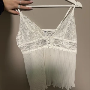 Vit spetslinne med plisserad nederdel - Fint vitt linne med spetsdetaljer och plisserad nederdel. Tunna axelband och fin spets upptill . 