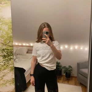 Vit t-shirt från Adidas - Säljer en klassisk vit t-shirt från Adidas med logotypen tryckt i svart på framsidan. T-shirten har en normal passform och korta ärmar.