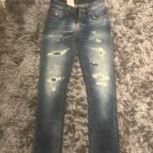 Blå ripped jeans från Nudie Jeans - Säljer dessa jeans från nudie pga var en julklapp som ej passade och returdatumet passerat. Jeansen är aldrig använda och skicket är 10/10. Passformen är slim och heter grim tim som syns på bild 4. Strl är 28 30. Jag säljer byxorna för 999 men ny pris är 1600 kr så en bra deal!
