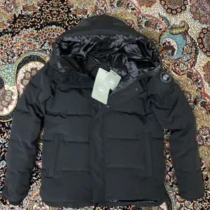 Canada Goose MacMillan Parks Black Label - Säljer en Canada Goose MacMillan Parka Black Label i storlek S. Jackan är i mycket fint skick och passar perfekt för dig som söker en kombination av stil och funktion i vinter. Den är svart, klassiskt designad och fylld med dun som håller dig varm även under de kallaste dagarna. Jackan är dessutom både vatten- och vindtät, vilket gör den idealisk för nordiskt klimat.