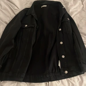 Svart jeansjacka med knappar - Snygg svart jeansjacka med silverfärgade knappar. Klassisk design med två bröstfickor och krage. Perfekt för en stilren look. Storlek xs men passar s/m
