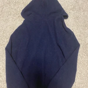 Mörkblå cashmere hoodie  - Säljer en stilren mörkblå kashmir hoodie med dragkedja och huva. Perfekt för kyliga dagar och enkel att matcha med andra plagg. Den har en praktisk dragkedja framtill och en bekväm passform. Nypris 900 kr