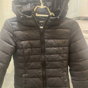 Svart pufferjacka från ONLY - Säljer en svart pufferjacka från ONLY i storlek XS. Jackan har en praktisk huva med dragsko och stängs med dragkedja. Perfekt för kyliga dagar.