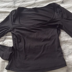 Svart långärmad topp - Snygg svart långärmad topp med en djup rundad halsringning. Perfekt för en stilren look och kan enkelt matchas med olika outfits.Aldrig nånsin använd