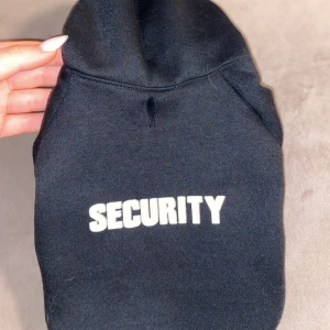 Svart hoodie med texten 'Security' till hundar  - Snygg svart hoodie med texten 'Security' i vitt på ryggen. Perfekt för en cool och avslappnad stil. Tröjan har en klassisk huva och korta ärmar. Här har vi en jätte skön tröja till hundar. Storlek S. använd 1 gång💕