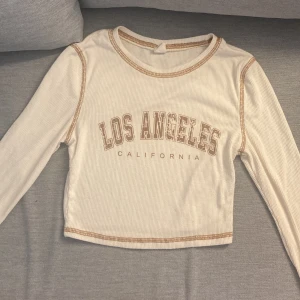 Vit ribbad tröja från Shein😍 - Säljer en vit ribbad tröja från Shein med texten 'Los Angeles California' på framsidan. Tröjan har långa ärmar och en croppad passform med kontrastsömmar i beige. Perfekt för en avslappnad stil!🛍️🎀