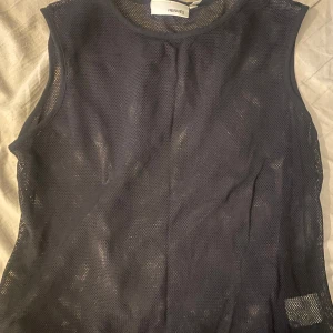 Svart ärmlös mesh-topp från Hennes - Snygg svart ärmlös topp i mesh från Hennes. Perfekt för lager-på-lager-stil eller som statement-plagg. Toppen har en rund halsringning och är tillverkad i ett lätt och luftigt material.