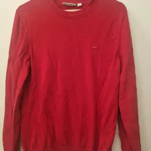 Röd tröja från Lacoste med rund halsringning och det klassiska krokodilmärket på bröstet.