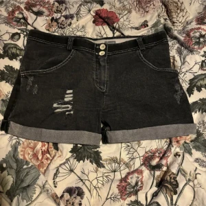 Svarta jeansshorts från Freddy - Snygga svarta jeansshorts från Freddy med slitna detaljer och uppvikta ben. Shortsen har två knappar i midjan och kontrasterande sömmar som ger en cool look. Perfekta för en avslappnad stil!