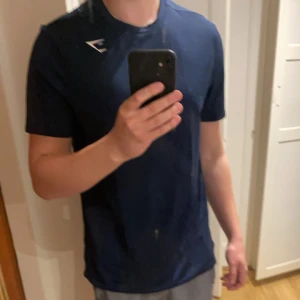 Mörkblå t-shirt från Gymshark - Snygg mörkblå t-shirt från Gymshark med en liten vit logga på bröstet. Perfekt för träning eller en avslappnad dag. T-shirten har en normal passform och är kortärmad.