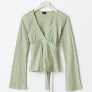 Grön omlottopp med knytband - Snygg grön omlottopp med långa ärmar och knytband i midjan, från Gina . Toppen har en v-ringad design. 