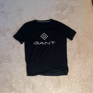 T-shirt  - Snygg svart t-shirt från GANT, säljer då den inte kommer till användning längrre. 9/10 skick. Perfekt för en stilren och avslappnad look. Passar ungdomar i storlek 176 cm. Hör av dig om du är intresserad🤍