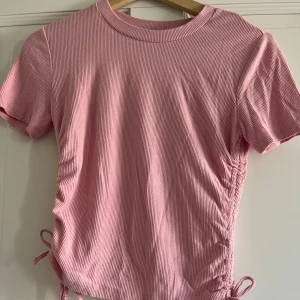 Rosa ribbad topp från Bik Bok - Säljer en rosa ribbad topp från Bik Bok i storlek XS. Den har korta ärmar och knytband på sidorna.