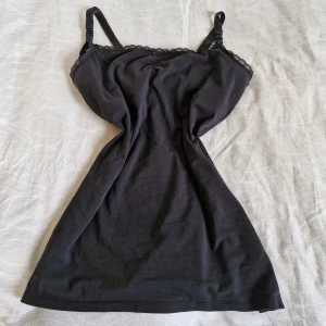 Svart linne med spetsdetaljer - Säljer ett svart linne med justerbara axelband och inbyggd "topp". Spetskant och rosett framtill. Det är gjort i ett mjukt och bekvämt material, perfekt för både vardag och fest. 