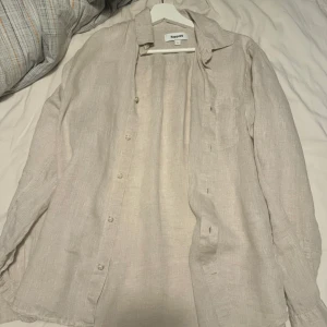 Beige linneskjorta från Kappahl - Säljer en snygg och luftig beige skjorta från Kappahl i storlek S. Skjortan är tillverkad i linne och har långa ärmar med knappar framtill. Perfekt för en avslappnad stil under vår och sommar!