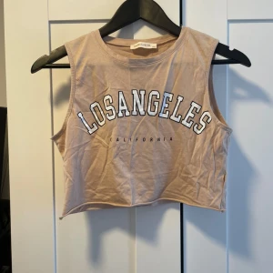 Beige croppad linnetopp från Barrels and Oil - Säljer en snygg beige croppad linnetopp från Barrels and Oil med texten 'Los Angeles California' tryckt på framsidan. Toppen är ärmlös och perfekt för en avslappnad sommarlook. Den är i bra skick och redo för nya äventyr!