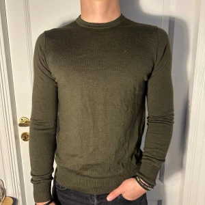 Olivgrön tröja från J.Lindeberg - Säljer en stilren olivgrön tröja från J.Lindeberg. Den är långärmad och har en normal passform. Tröjan är i Väldigt bra skick! Modellen är 182 cm och väger 75 kg. Priset är öppen till förhandling!